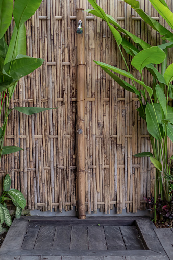 Vertical shot of an outdoor shower in tropical villa resort, with bamboo wall and faucet.