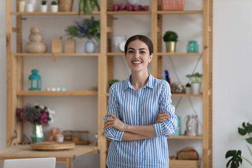 Young businesswoman in casual elegant blouse posing in office with arms crossed smile look at camera feel satisfied by career in company. Independent woman portrait, teacher pose at workplace concept