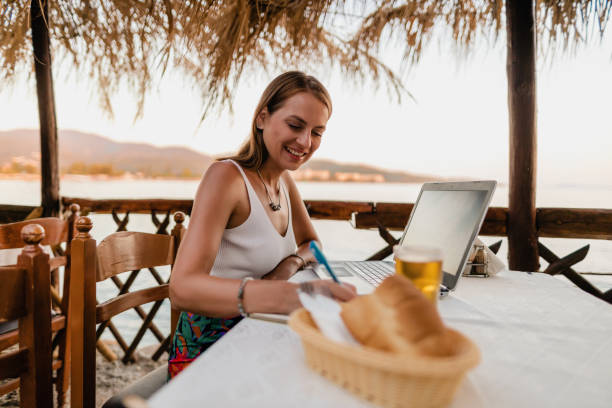 istock Young woman using a laptop in a restaurant at the seaside 1415008184