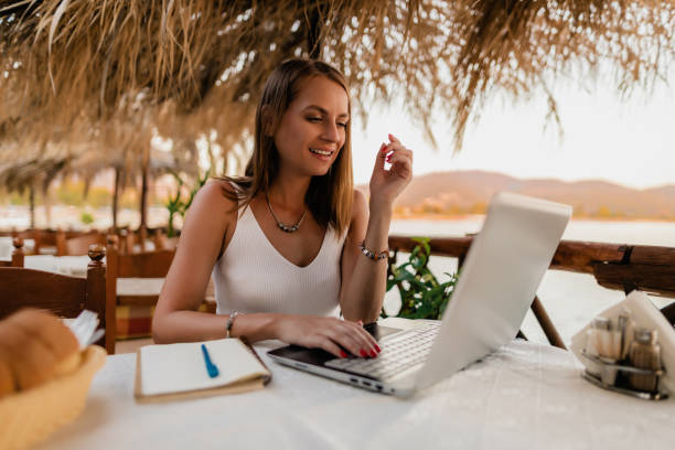 istock Young woman using a laptop in a restaurant at the seaside 1415008186