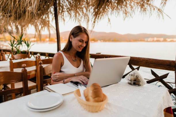 istock Young woman using a laptop in a restaurant at the seaside 1415008227