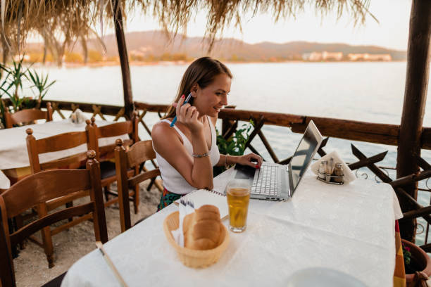 Woman studying and doing homework during seaside vacation Smiling young woman sitting in a restaurant at the seaside, using a laptop and doing homework during summer vacation halkidiki beach stock pictures, royalty-free photos & images