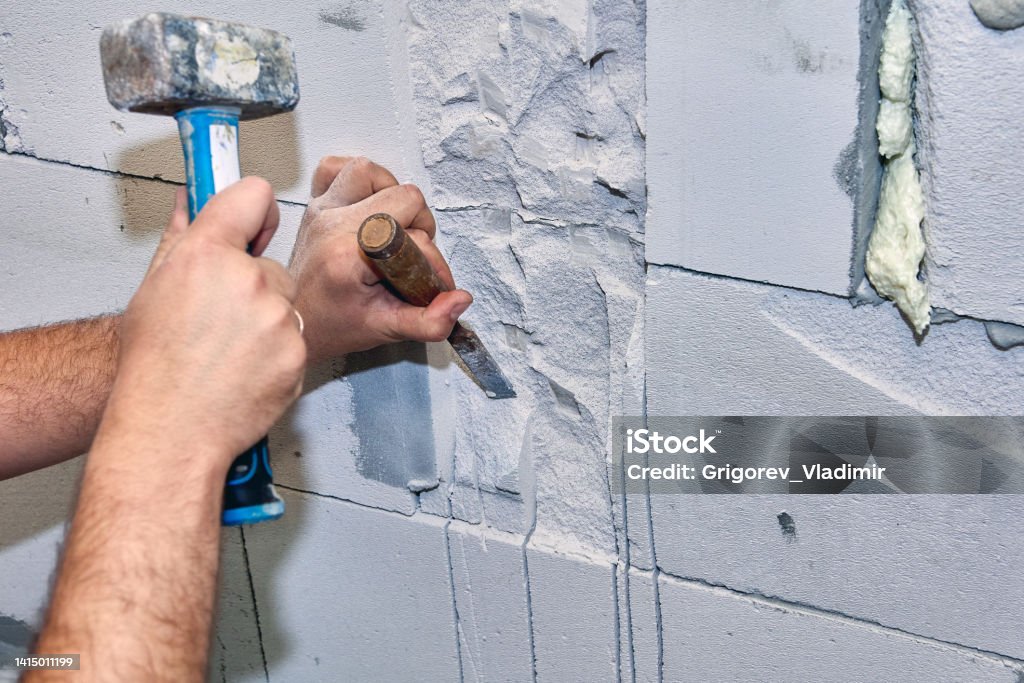 Construction worker gouges niche in concrete wall using hammer and chisel. Builder gouges niche in masonry using hammer and chisel. Apse Stock Photo