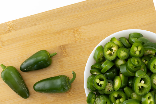 Still life with fresh sliced jalapeno pepper in white bowl and wooden board. Green organic chili pepper. Kitchen background. Top view, selective focus