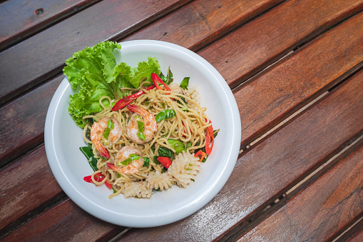 Flat lay of stir fried spicy spaghetti with seafood on wooden tabletop in vintage tone style