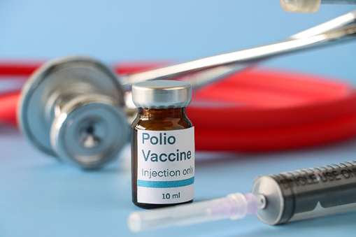 Imagen de primer plano del vial de vidrio etiquetado de la vacuna contra la poliomielitis (poliovirus) junto con una jeringa y un estetoscopio, fondo azul, enfoque en primer plano, espacio de copia photo
