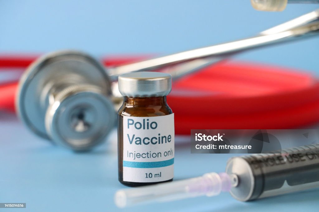 Close-up image of Polio (Poliovirus) vaccine labelled glass vial besides a syringe and stethoscope, blue background, focus on foreground, copy space Stock photo showing close-up view of stethoscope and syringe besides a labelled glass vial of Polio (Poliovirus) vaccine. Polio Vaccine Stock Photo