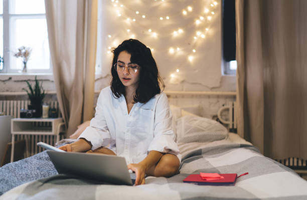 istock Focused woman using laptop on bed in cozy bedroom 1415014816