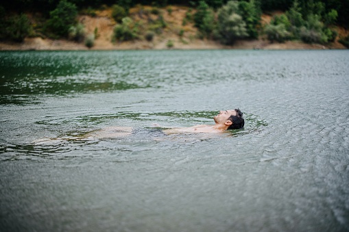 A 10-year-old boy in green swimming goggles swims in the sea near the shore