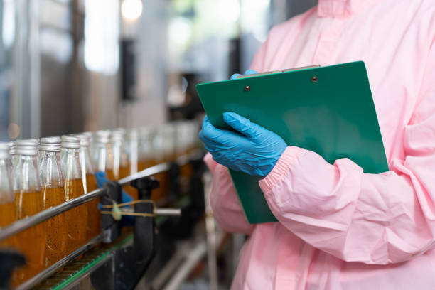 istock Hands of worker writing notes on clipboard check product of Basil seed with fruit on the conveyor belt in the beverage factory. Worker checking bottling line for processing. Inspection quality control 1415018630