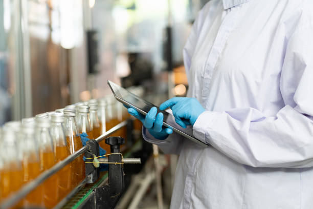 mani di lavoratore che lavora con il prodotto di controllo del tablet digitale sul nastro trasportatore nella fabbrica di bevande. operaio che controlla la linea di imbottigliamento per la lavorazione. controllo qualità dell'ispezione - industry repairing computer technology foto e immagini stock