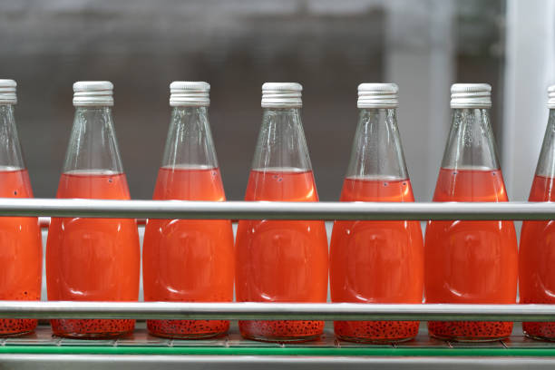 producto de jugo de fruta en la cinta transportadora en la fábrica de bebidas. línea de embotellado para el procesamiento y embotellado de semillas de albahaca con fruta en botellas. industria de alimentos, salud y bebidas - bottling plant industry drink food processing plant fotografías e imágenes de stock