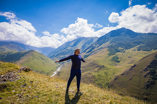 A man stands on top of a mountain with arms outstretched, North Ossetia, the village of Kamunta.