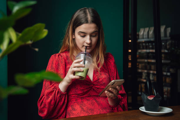 young woman drinking green drink ice matcha latte in cafe and using smartphone. - blueberry smoothie milk shake drink imagens e fotografias de stock