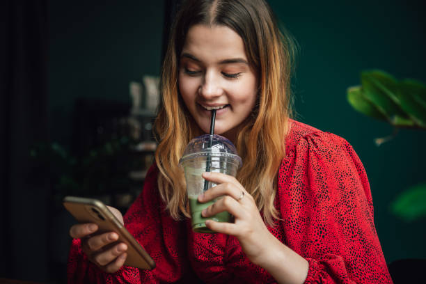 young woman drinking green drink ice matcha latte in cafe and using smartphone. - blueberry smoothie milk shake drink imagens e fotografias de stock
