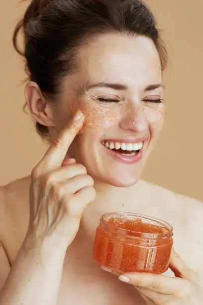 smiling modern 40 years old woman with face scrub on beige background.