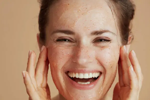 Photo of happy modern woman with face scrub against beige background