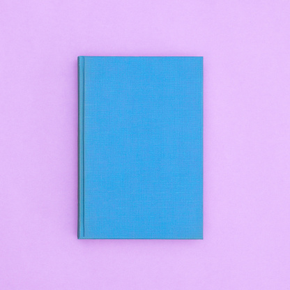 Blue hardcover vintage book on pastel purple background. Flat lay copy space