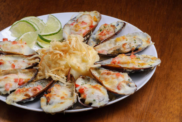 Baked mussels au gratin with mashed potatoes on a white plate on wooden table. Brazilian seafood. Baked mussels au gratin with mashed potatoes on a white plate on wooden table. Brazilian seafood. seafood gratin stock pictures, royalty-free photos & images