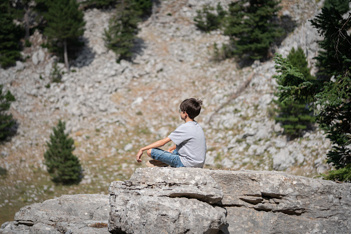 A boy traveler with hiking poles and a backpack is resting in the summer on top of a mountain with snow. Mountain peak in the summer. Caucasus, Russia