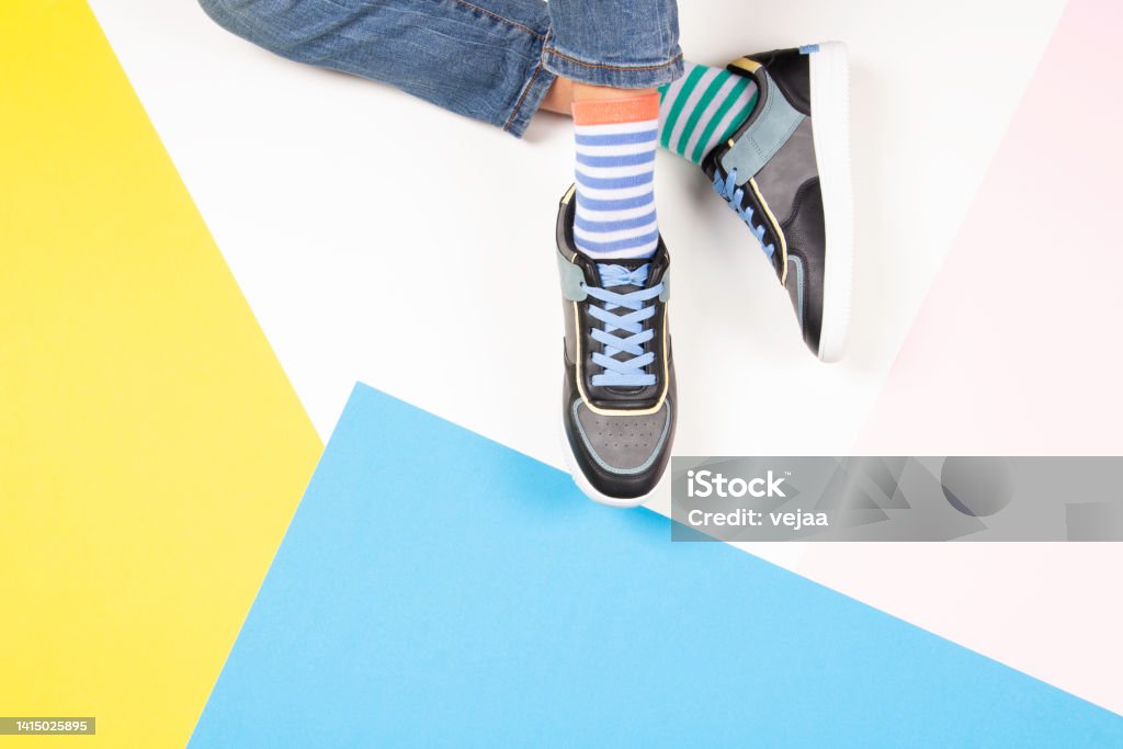 Kid wearing different pair of socks. Child foots in mismatched socks and colorful sneakers sitting on white background. Top view. Odd Socks day, Anti-Bullying Week, Down syndrome awareness concept Kid wearing different pair of socks. Child foots in mismatched socks and colorful sneakers sitting on white background. Top view. Odd Socks day, Anti-Bullying Week, Down syndrome awareness concept. Canvas Shoe Stock Photo