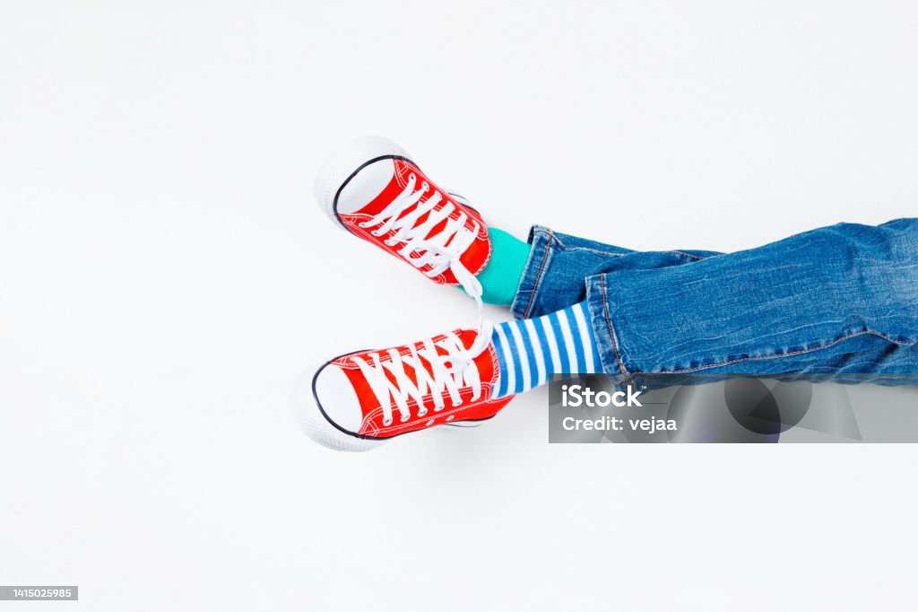 Kid wearing different pair of socks. Child foots in mismatched socks and red sneakers sitting on white background. Odd Socks day, Anti-Bullying Week, Down syndrome awareness concept Kid wearing different pair of socks. Child foots in mismatched socks and red sneakers sitting on white background. Odd Socks day, Anti-Bullying Week, Down syndrome awareness concept. Child Stock Photo