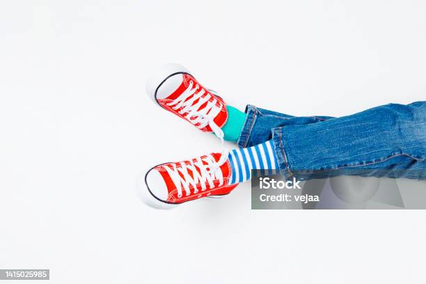 Kid Wearing Different Pair Of Socks Child Foots In Mismatched Socks And Red Sneakers Sitting On White Background Odd Socks Day Antibullying Week Down Syndrome Awareness Concept Stock Photo - Download Image Now