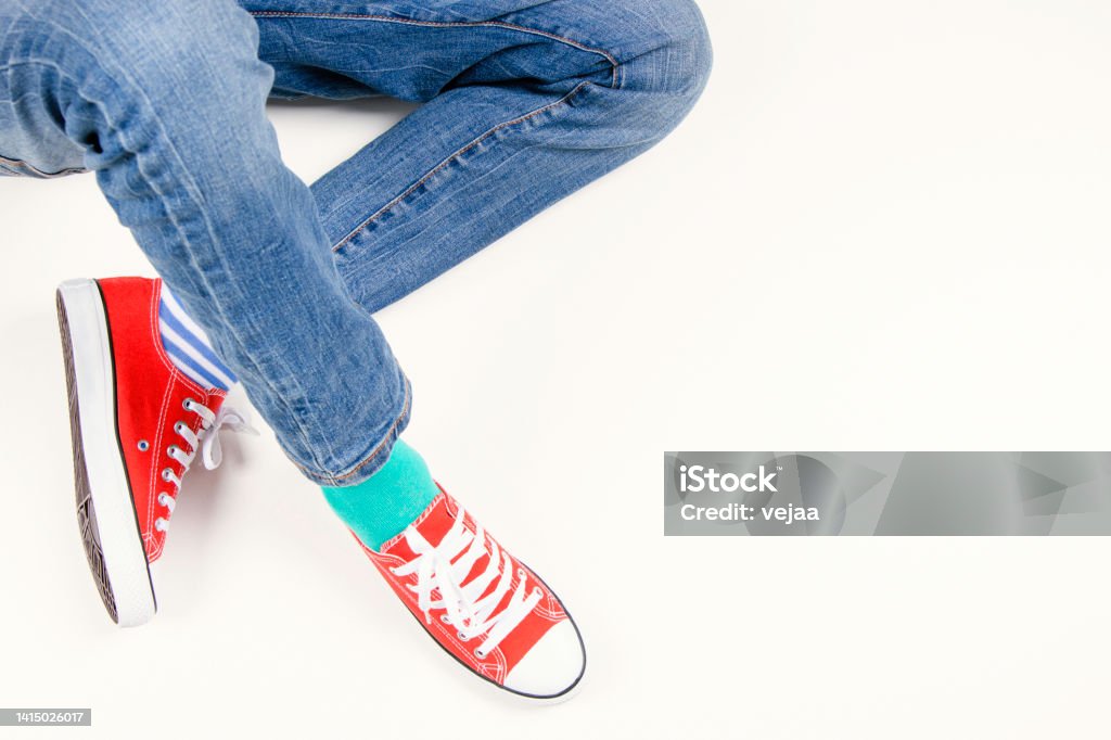 Kid wearing different pair of socks. Child foots in mismatched socks and red sneakers sitting on white background. Odd Socks day, Anti-Bullying Week, Down syndrome awareness concept Kid wearing different pair of socks. Child foots in mismatched socks and red sneakers sitting on white background. Odd Socks day, Anti-Bullying Week, Down syndrome awareness concept. Above Stock Photo