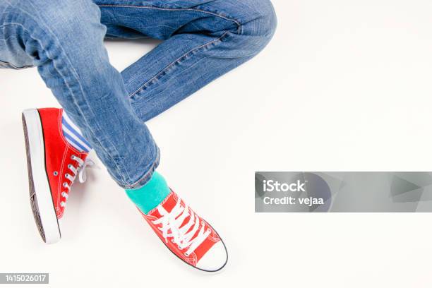 Kid Wearing Different Pair Of Socks Child Foots In Mismatched Socks And Red Sneakers Sitting On White Background Odd Socks Day Antibullying Week Down Syndrome Awareness Concept Stock Photo - Download Image Now