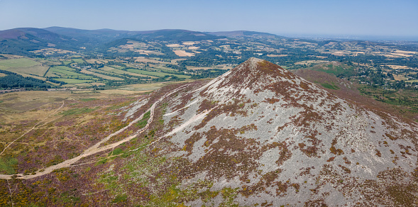 Drone aerial view of Sugarloaf mountain, County Wicklow, Ireland, on a hot sunny summer day with blues skies and green fields in the distance, shot in panoramic. The mountain is very popular with hikers and walkers and is a tourist attraction, and this shows the southern side of the mountain
