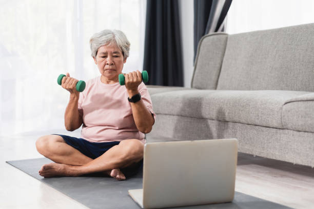 koncepcja uczenia się dorosłych online, azjatycka starsza kobieta ucząca się podnosić hantle. z przewodnika wideo na laptopie. - floor women sitting yoga zdjęcia i obrazy z banku zdjęć