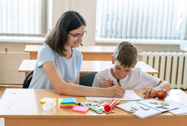 istock A boy and a teacher doing homework, writing text in a notebook at the table. A mother helps her son write in a notebook 1415029926