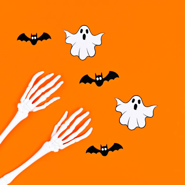 istock Skeleton hands with bats and ghosts on orange background. Flat lay 1415033870