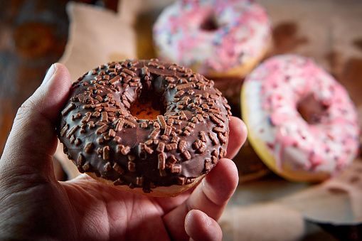the close-up of a chocolate donut in a human hand, blurred background