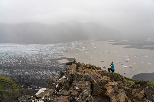 One women standing and taking photo with mobile phone on rock at Skaftafell Glacier in Vatnajokull National Park, South Iceland