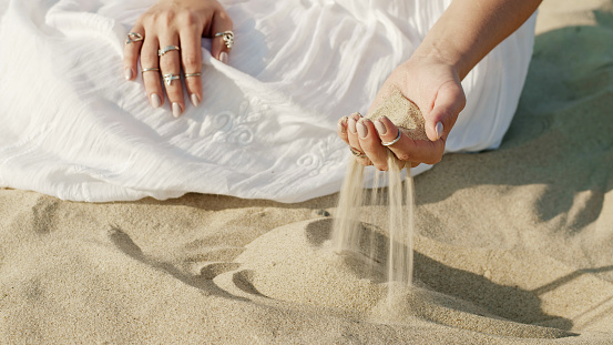 Woman hands playing with sand at beach. Time passes. Beautiful scene of young boho gypsy girl in white dress with rings touching grit. High quality photo