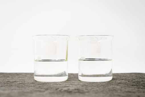 Two beakers with clear liquids and blank labels against white background