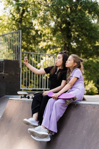 スケートボードとペニーボードを持つ電話中毒のスポーツの子供たちは、スケートや一緒に遊ぶ代わりに、携帯電話を使用して自分撮りを作ります。スポーツランプでスマホを見ている子ど� - skateboard park ramp park skateboard ストックフォトと画像