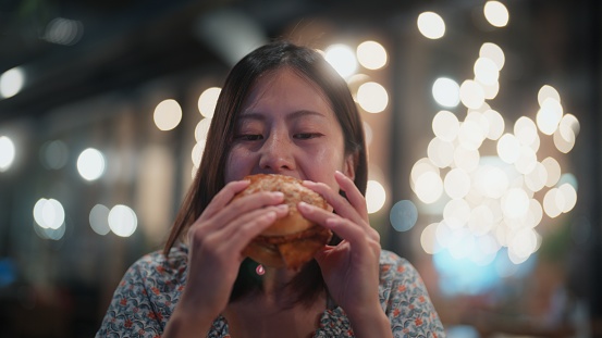 A young woman is enjoying eating hamburger for dinner in a restaurant.