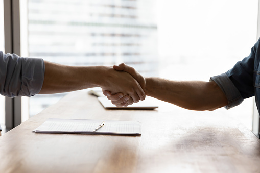 Two businessmen shaking hands over conference table in office. Business partners, client and lawyer giving handshakes after meeting. Employer hiring employee after job interview. Close up