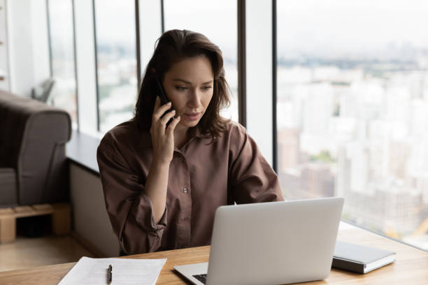 Serious businesswoman talking on mobile phone at office workplace