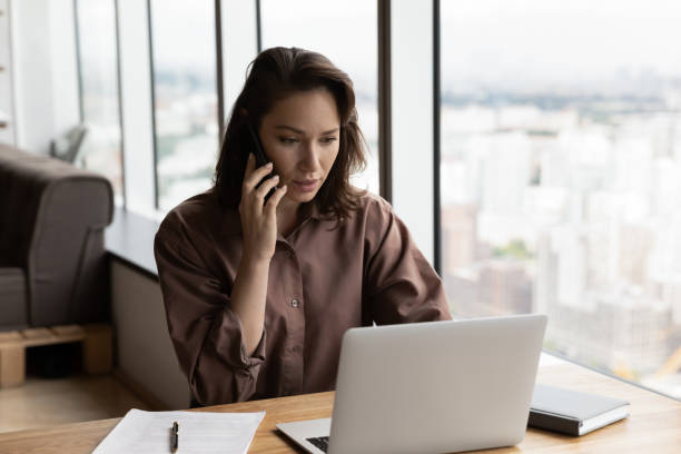 Serious businesswoman talking on mobile phone at office workplace stock photo