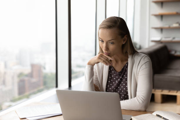 istock Thoughtful businesswoman working at laptop, reading text on screen 1415053268