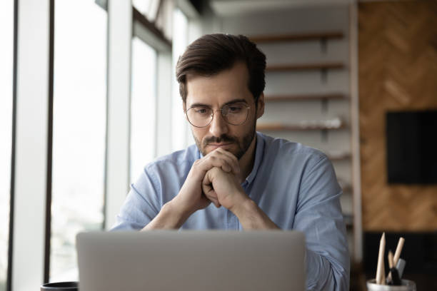 thoughtful focused business man in glasses working at laptop computer - computer thinking men people imagens e fotografias de stock