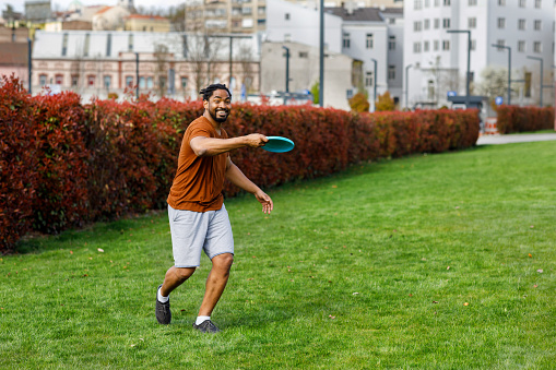 Handsome African Man is Throwing a Frisbee and Enjoying in Summer Day with Friends.