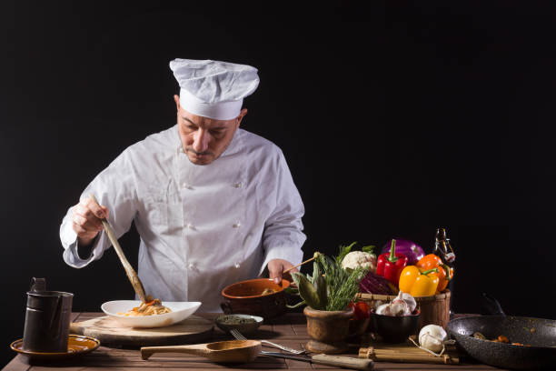 istock Male chef in white uniform prepares spaghetti with vegetables on the dish 1415055611