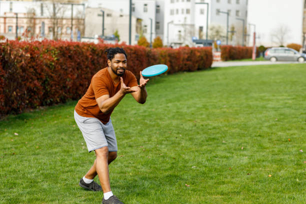 un joven africano está cogiendo un frisbee mientras juega con amigos en un parque. - grave nature usa city life fotografías e imágenes de stock