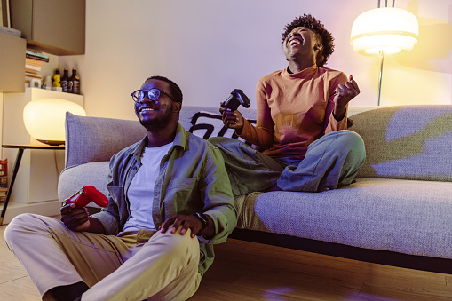 Side view of a cheerful young couple playing video games and having fun at home. Leisure game night at home