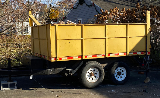Side view of a large yellow dupmster on a trailer in a residential driveway for garbage from home renovation to be placed in.