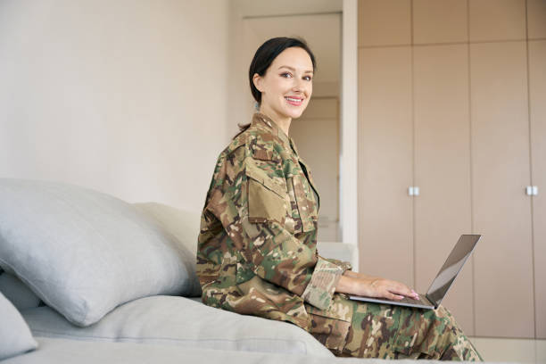 istock Smiling female infantryman sitting on sofa with laptop 1415063775